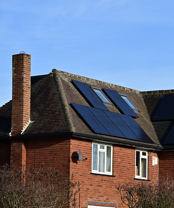 red brick house with solar panels on the roof featuring nine panels and a chimney against a clear blue sky