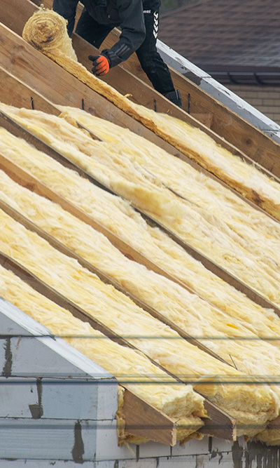 person installing insulation on a sloped roof with yellow fiberglass material for improved energy efficiency in home construction