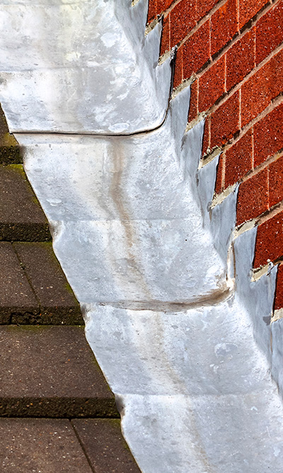 close up of a metal flashing along a brick wall and pavement highlighting the transition between materials crucial for effective water drainage and protection against moisture damage in seven areas