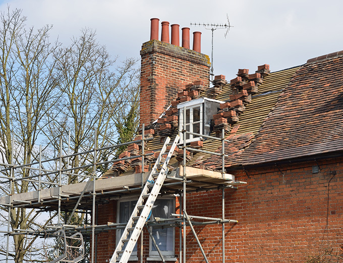 a house under renovation with scaffolding and a ladder leading up to a partially repaired roof featuring brick chimneys and trees in the background significant home improvement 15 renovation ideas