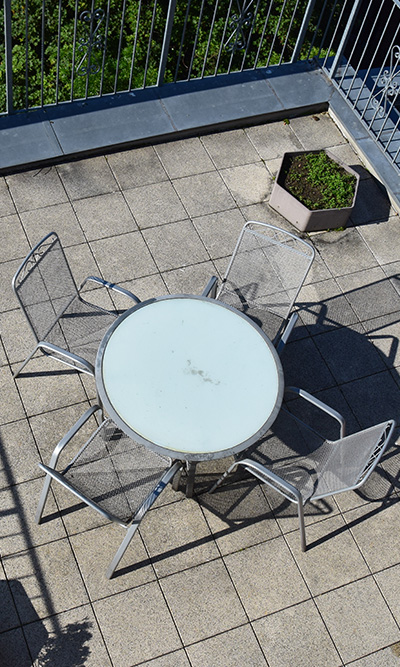 round glass table with four metal chairs on a patio area featuring green plants suitable for a gathering of friends or family enjoying a relaxed outdoor setting with up to 13 people